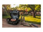 Electric grill with steak and spices on a wooden table in a garden setting.