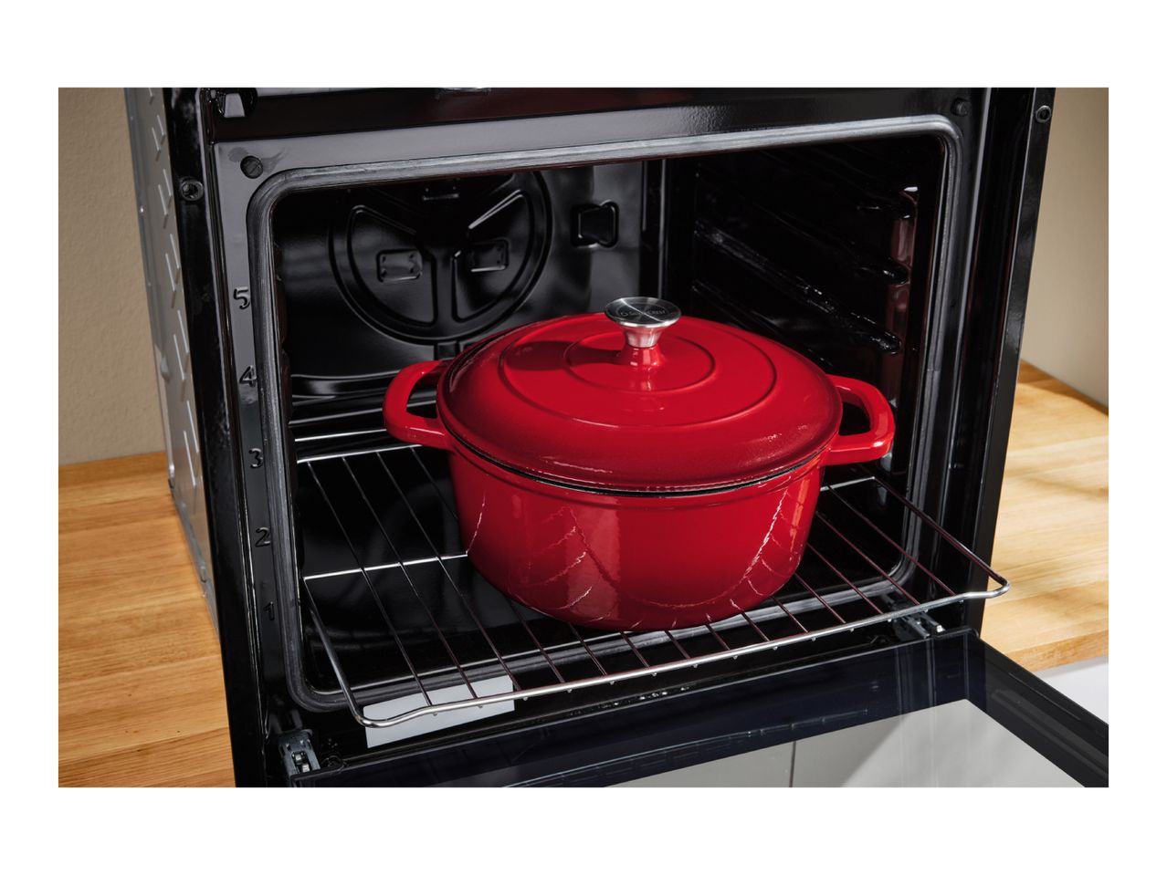 Red SilverCrest Dutch oven inside a black oven on a rack.