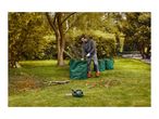 Man in garden clearing branches into green garden waste bags with a chainsaw nearby.