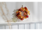 Autumn wreath with pumpkins and leaves, and a glass candle holder on a white shelf.