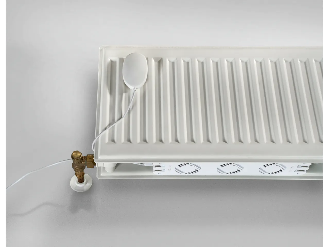 A white radiator with a smart thermostat and a fan booster attached to its bottom.