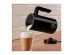 Black milk frother pouring foam into a glass of latte on a wooden counter.
