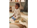 Baby in a knitted jumpsuit and blue socks playing with wooden toys on a rug.