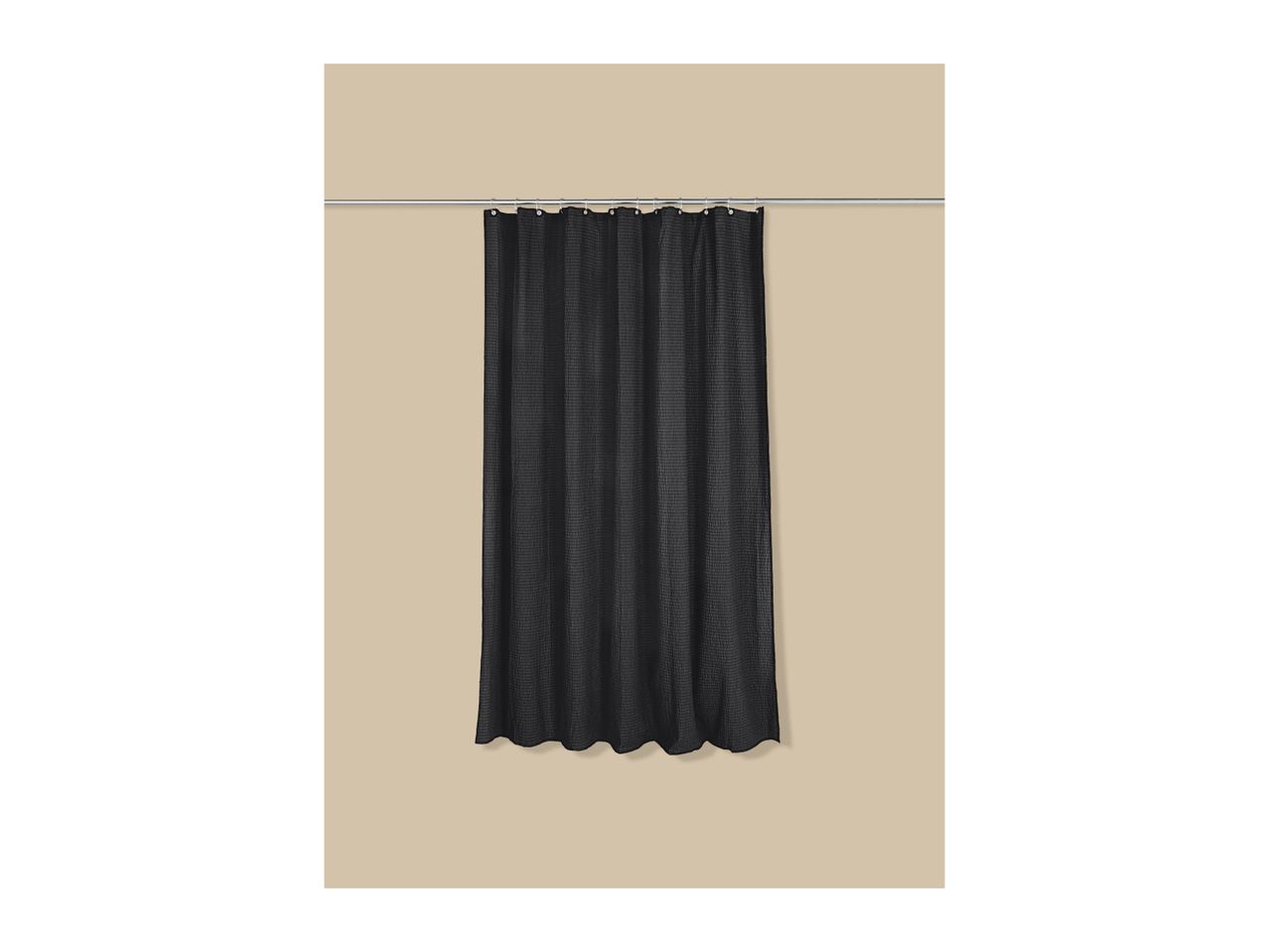 Black waffle-textured shower curtain hanging on a silver rod against a beige wall.