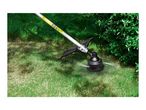 A grass trimmer cutting grass in a garden, with safety labels visible on the shaft.