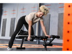 Woman in Crivit® sports shirt and leggings doing a dumbbell row on a bench.
