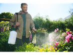 Man using a Parkside® garden sprayer to water plants in a sunny garden.