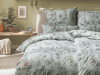 Ein Bett mit floraler Bettwäsche in einem Schlafzimmer mit Pflanzen und einem Wecker auf einem Nachttisch.