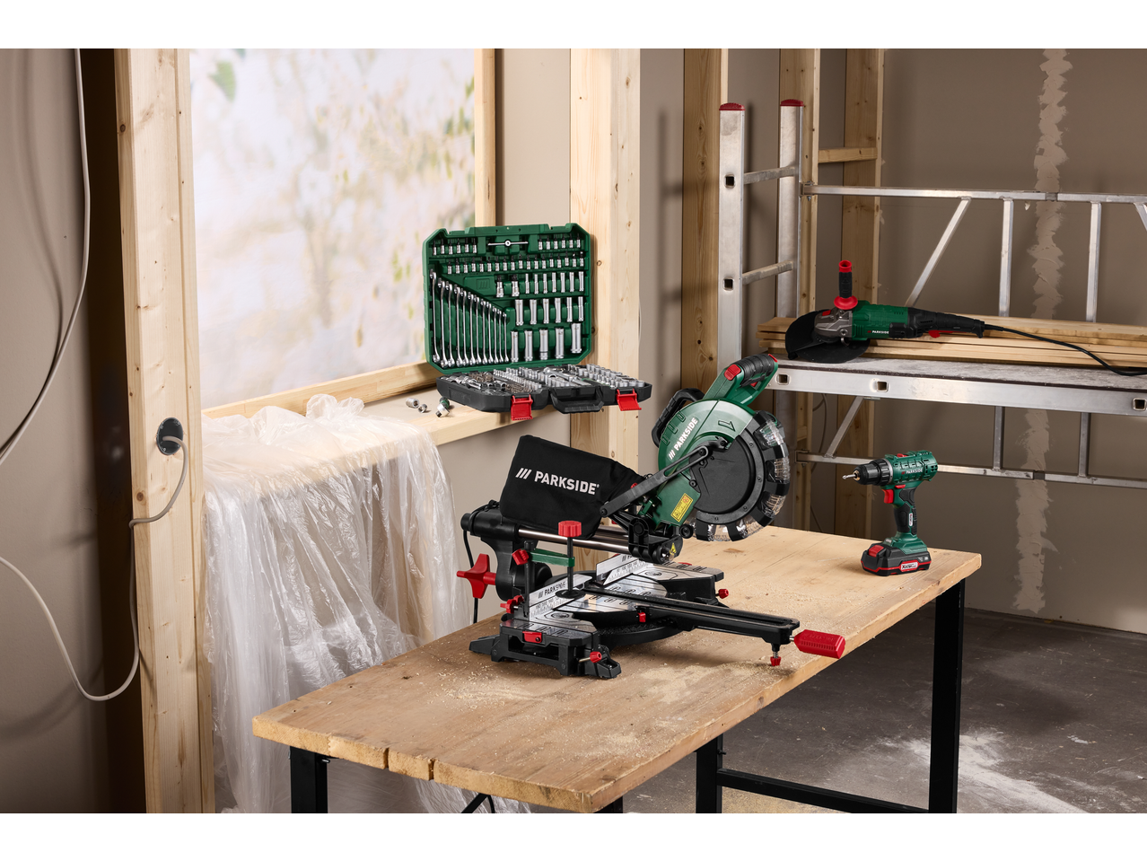 PARKSIDE® angle grinder, miter saw, and drill on a workbench with a tool set.