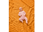 Baby in a pink lupilu® sleepsuit lying on an orange blanket.