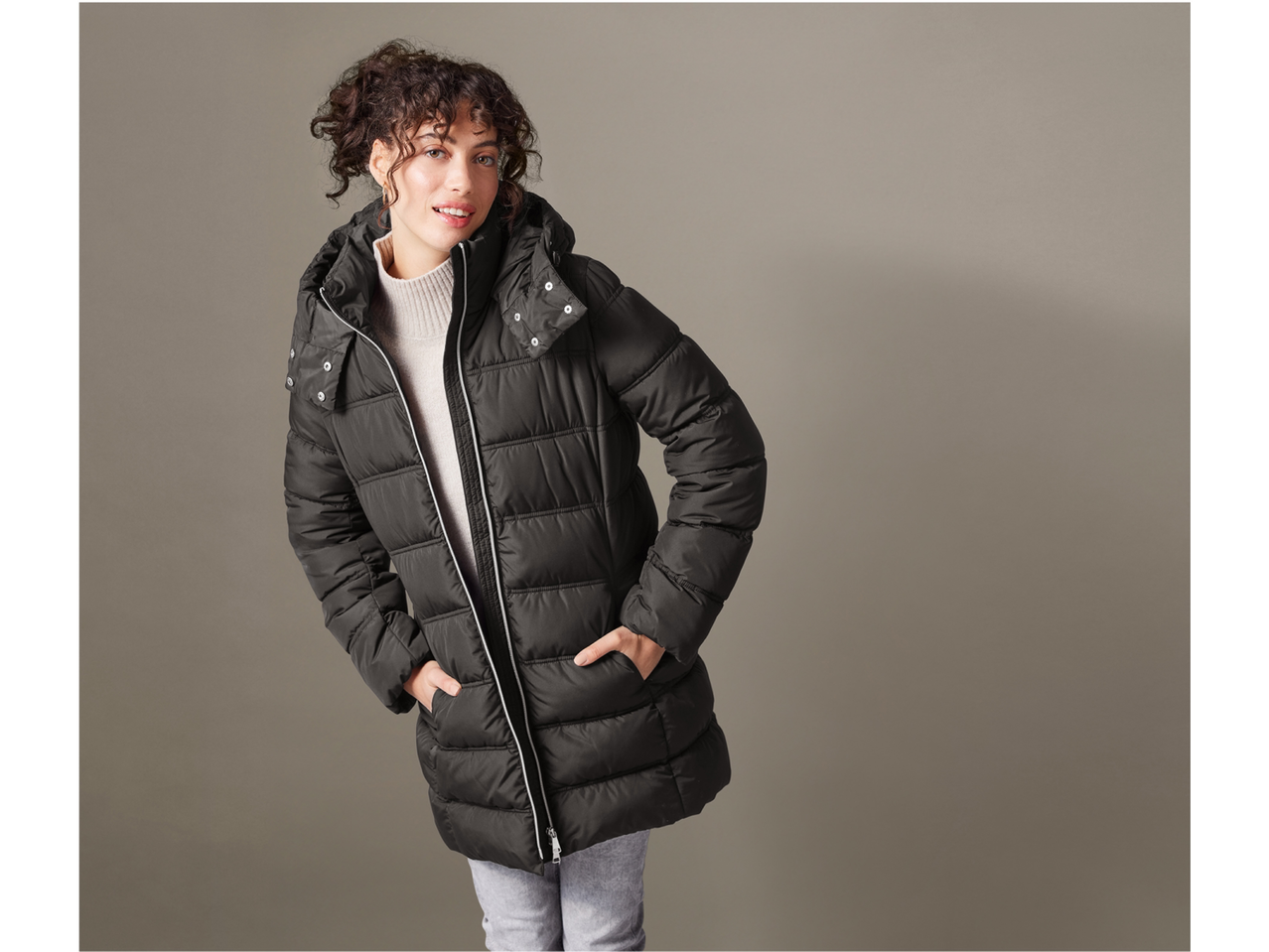 Moteris su juodu esmara® dygsniuotu paltu su gobtuvu ir smėlio spalvos golfu.