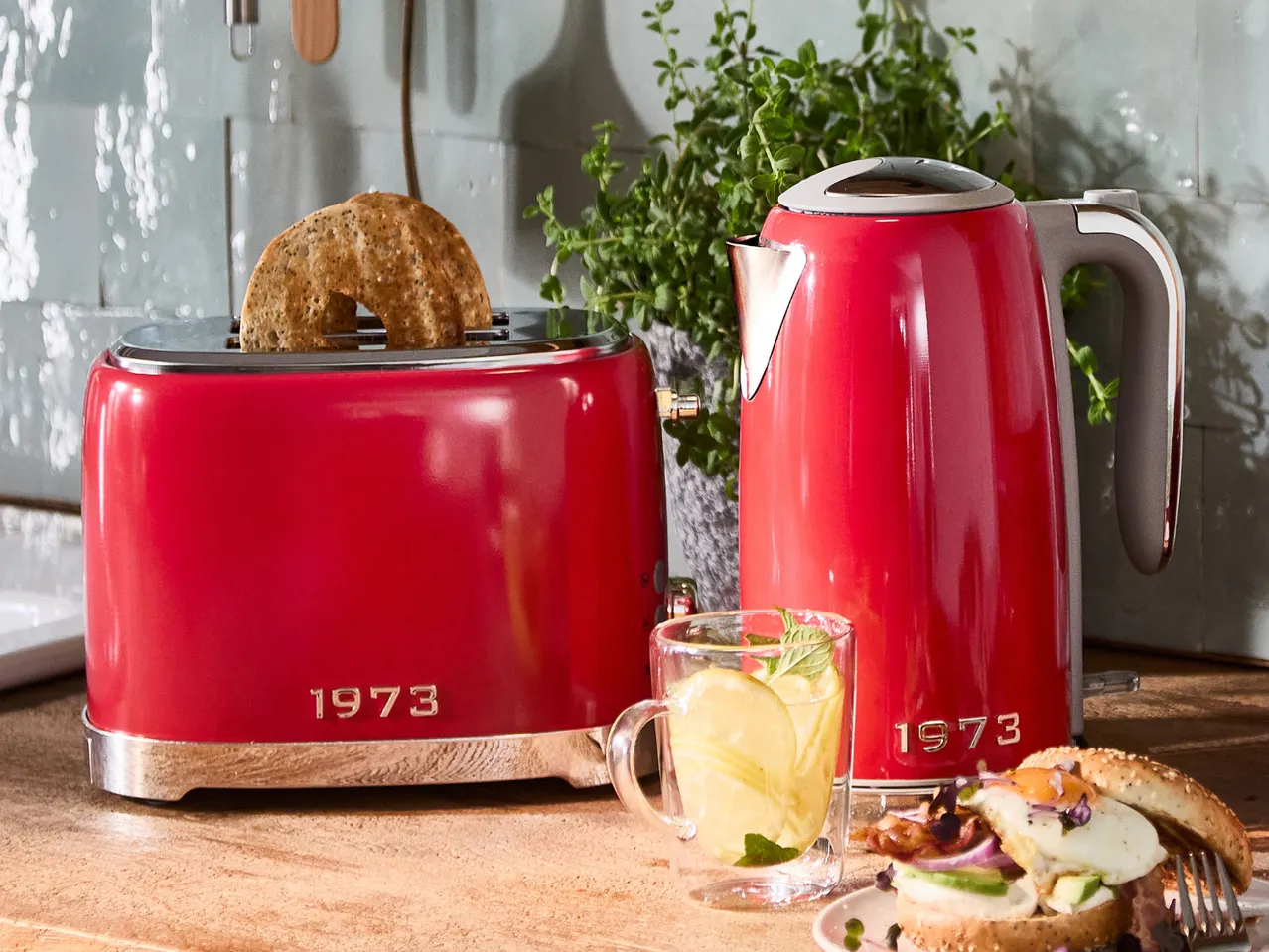 Red 1973 branded toaster and kettle on a kitchen counter with breakfast items.