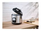 A stainless steel rice cooker with cooked rice on a wooden countertop.