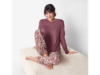 Smiling woman in Esmara pajamas with paisley patterned pants, sitting on an ottoman.
