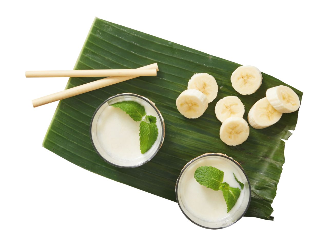 Banana smoothies with mint and sliced bananas on a banana leaf with bamboo straws.