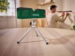 A Parkside laser level on a tripod, projecting red lines onto a wall where a man is working.