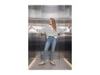 Woman in striped sweater, jeans, and sneakers in an elevator.