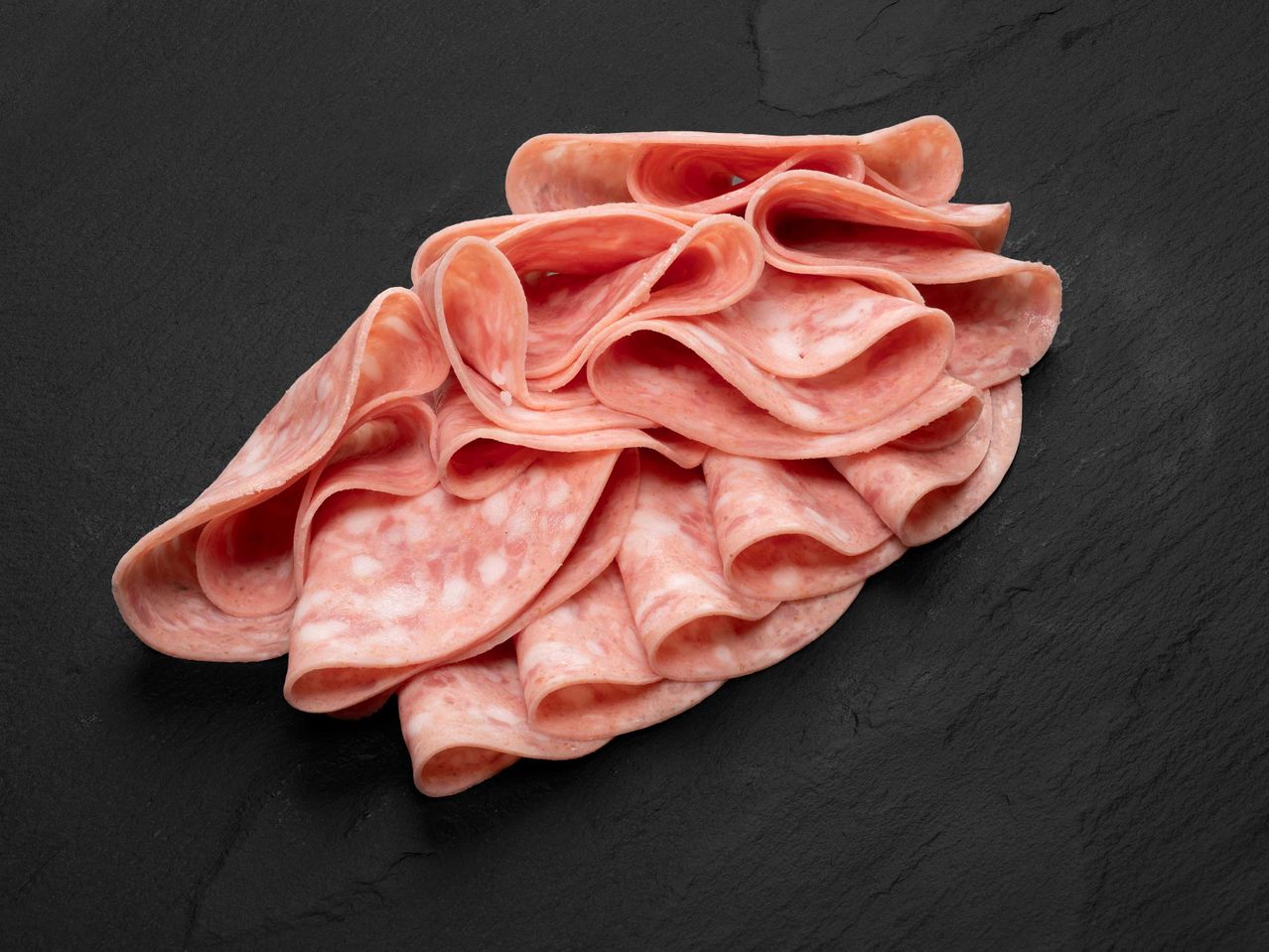 Feltekert, szeletelt szalámi fekete palatáblán.