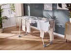 Clothes drying rack with various garments in a bright room with wooden floor and plants.