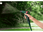 Mão segurando uma mangueira verde PARKSIDE Flexi-Gartenschlauchset, 30 m, a pulverizar água num jardim.