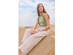 Woman in green sleeveless top and beige trousers sitting on sand dunes.