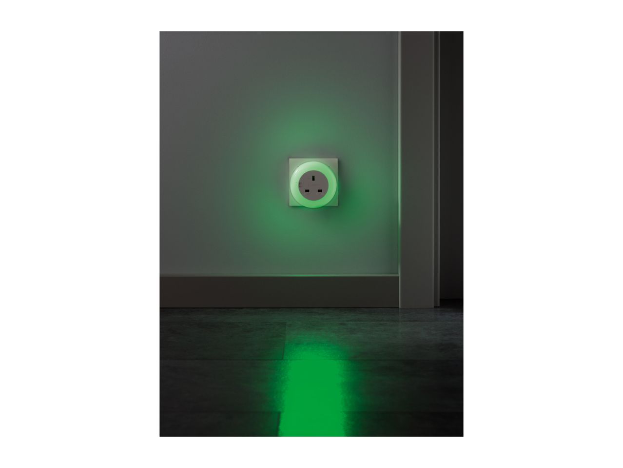 A night light plugged into a wall socket, casting a green glow on the wall and floor.