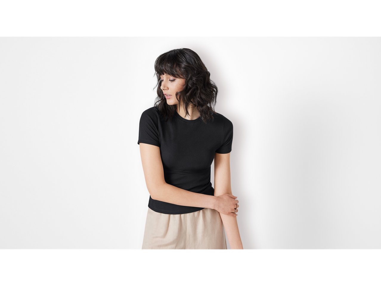 Žena modelira crnu rebrastu majicu i bež hlače.