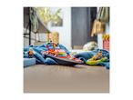 Toy fireboat and small green boat with minifigures on a blue blanket and wooden floor.