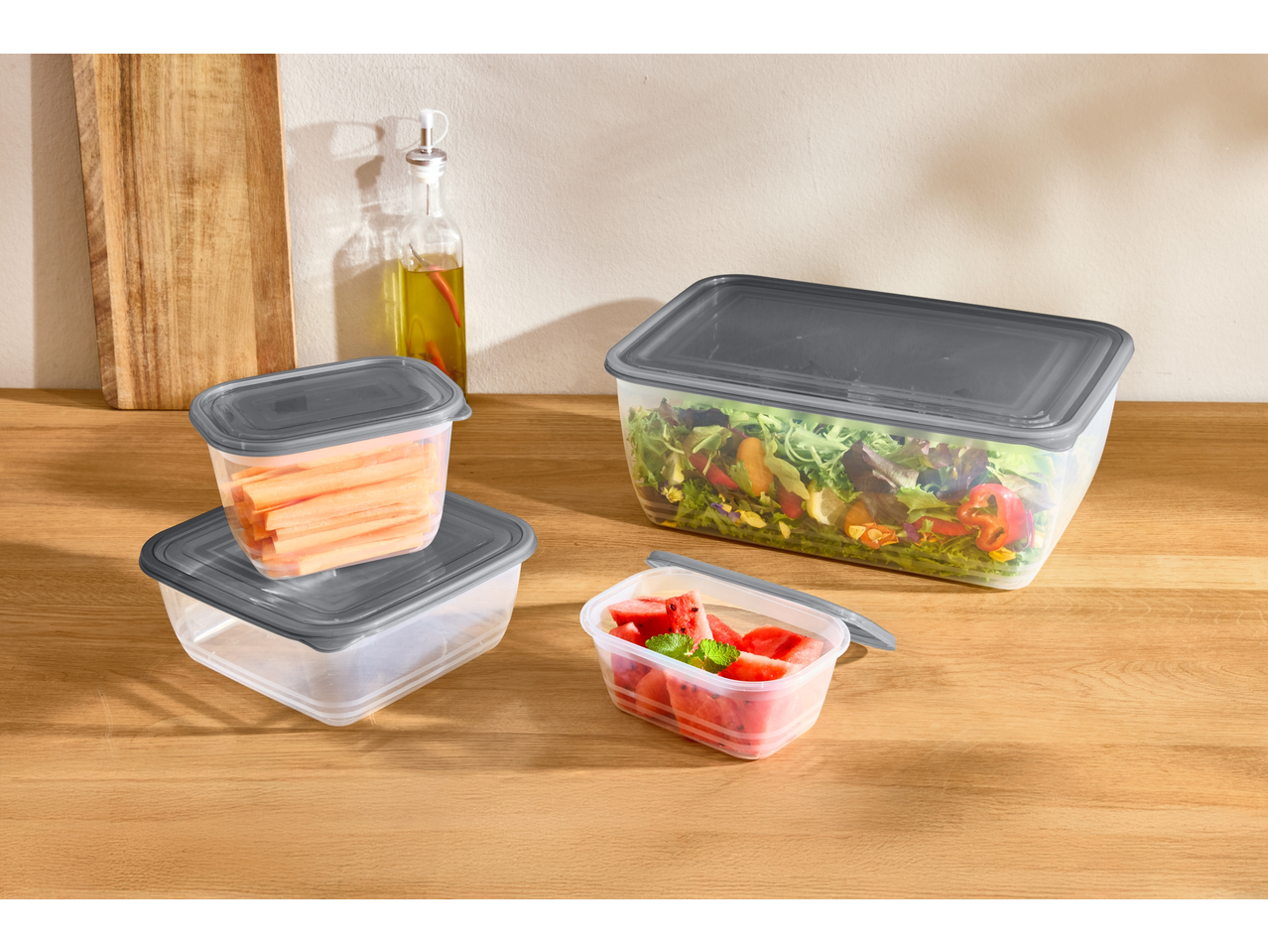 Posude za hranu sa salatom, šargarepom i lubenicom na drvenom pultu.