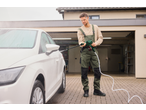 Man in overalls and safety glasses pressure washing a white car with a cordless pressure washer.