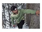 A man wearing a head torch and a green outdoor jacket in a snowy forest.