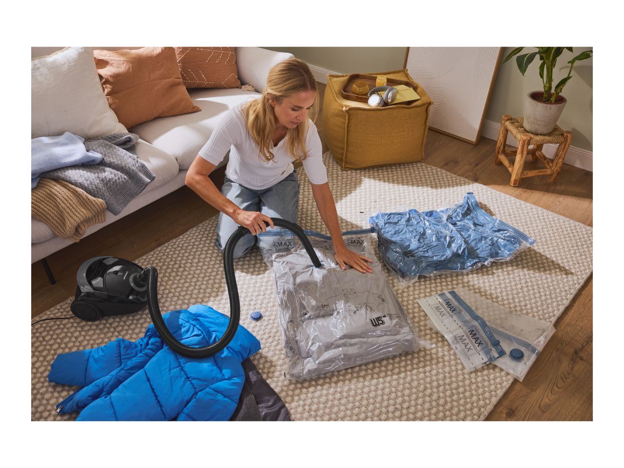 Woman using a vacuum cleaner to seal clothes in vacuum storage bags on a rug.