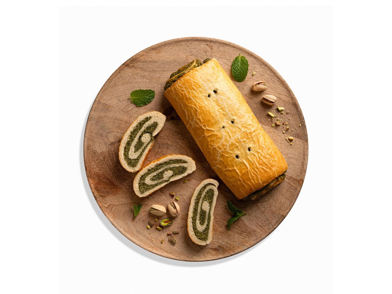 Pistáciás tekercs mentával és pisztáciával díszítve, fa tálcán.