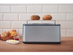 Stainless steel toaster with two bread rolls on top, next to a bowl of bread, jam, and butter.