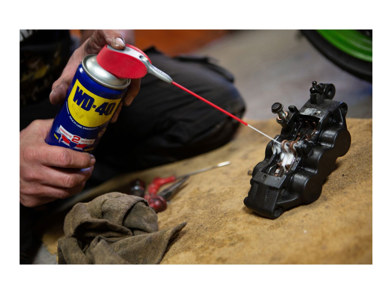 Person cleaning a brake caliper with a spray lubricant.
