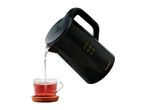 Black electric kettle pouring water into a glass cup of red tea on a cork coaster.