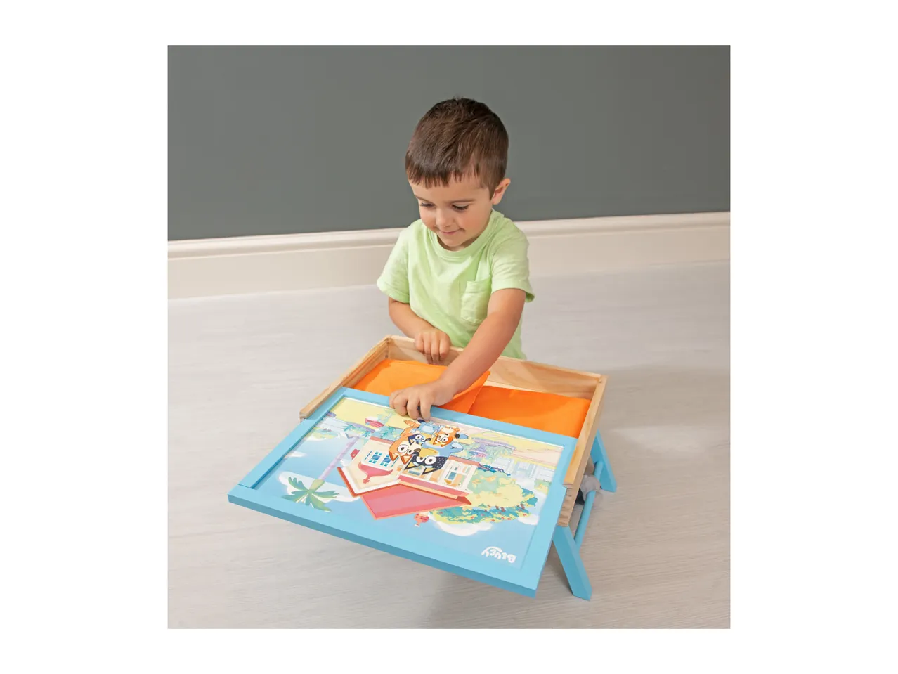 A child playing with a wooden activity tray featuring a cartoon town scene.