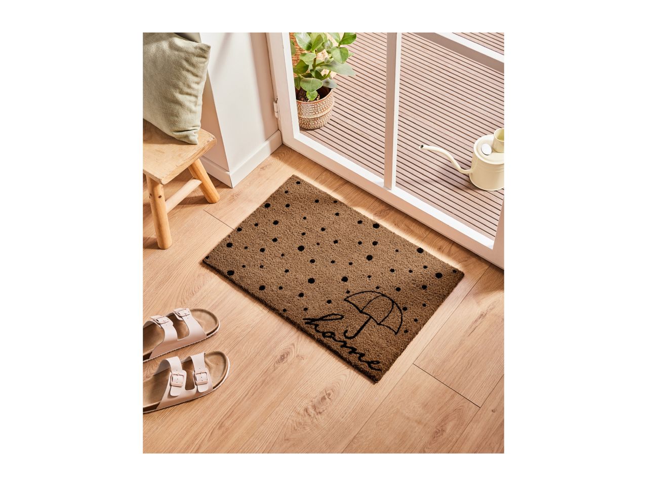 A brown doormat with black polka dots and an umbrella design, with sandals nearby.