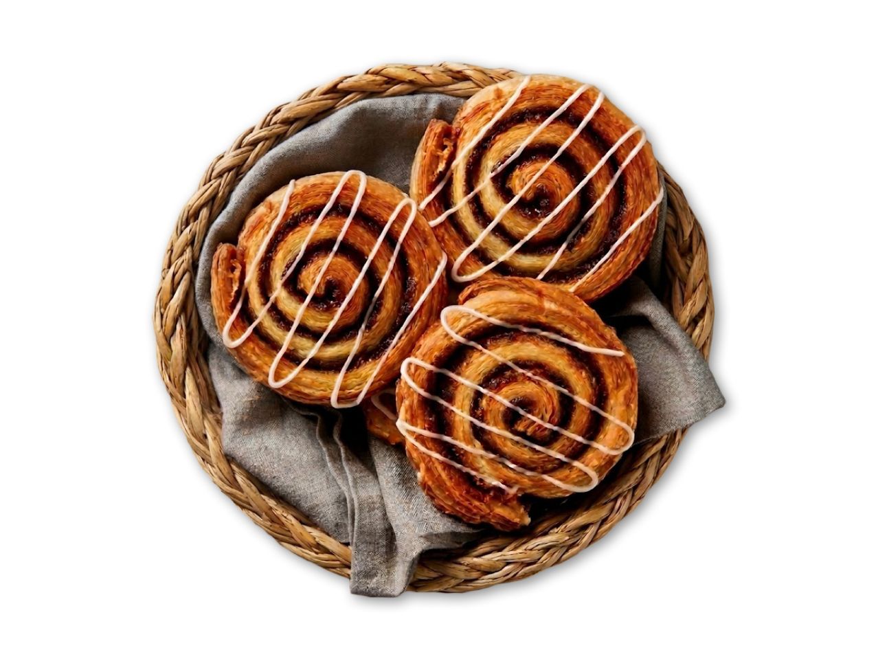 Tre kanelsnegle med hvid glasur i en flettet kurv med et gråt klæde.