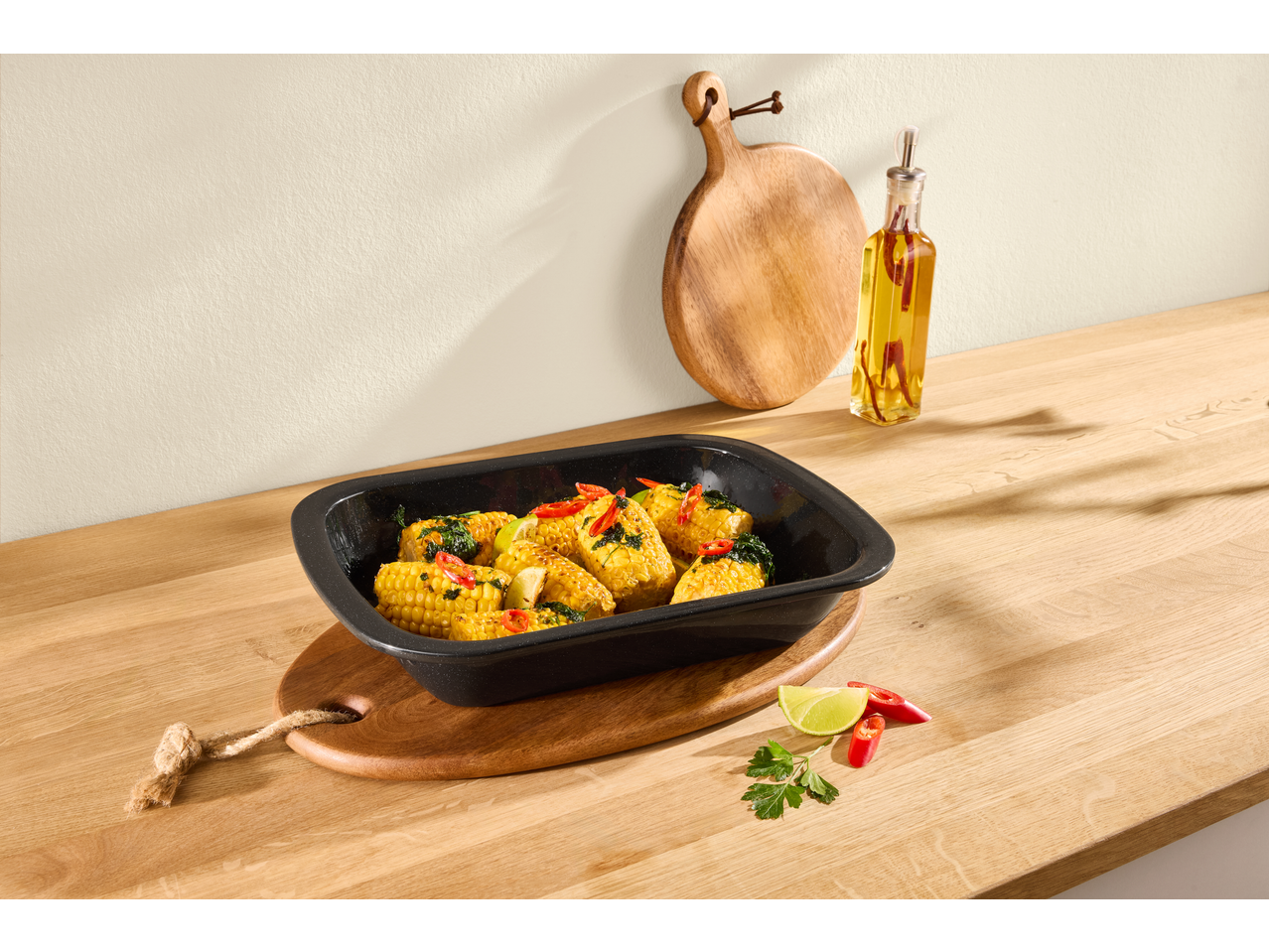 Roasted corn on the cob with herbs and chili in a black baking dish on a wooden countertop.