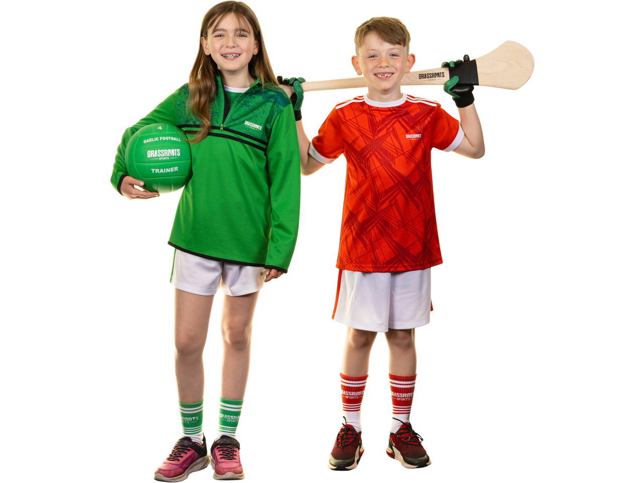 Two children in sports gear, a girl in green holding a Gaelic football and a boy in red with a hurley.