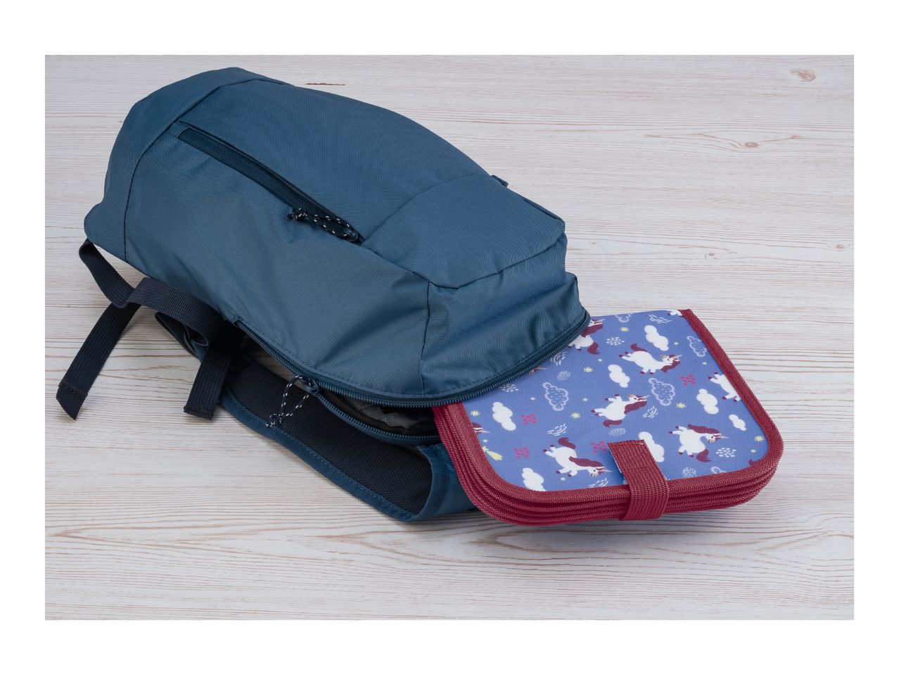 A blue backpack with a unicorn-themed pencil case partially unzipped on a light wooden surface.
