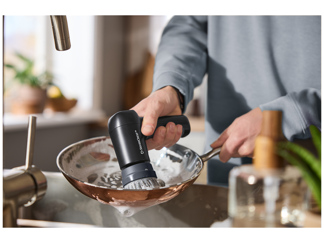 Une personne lave une poêle avec une brosse de nettoyage électrique dans un évier de cuisine.
