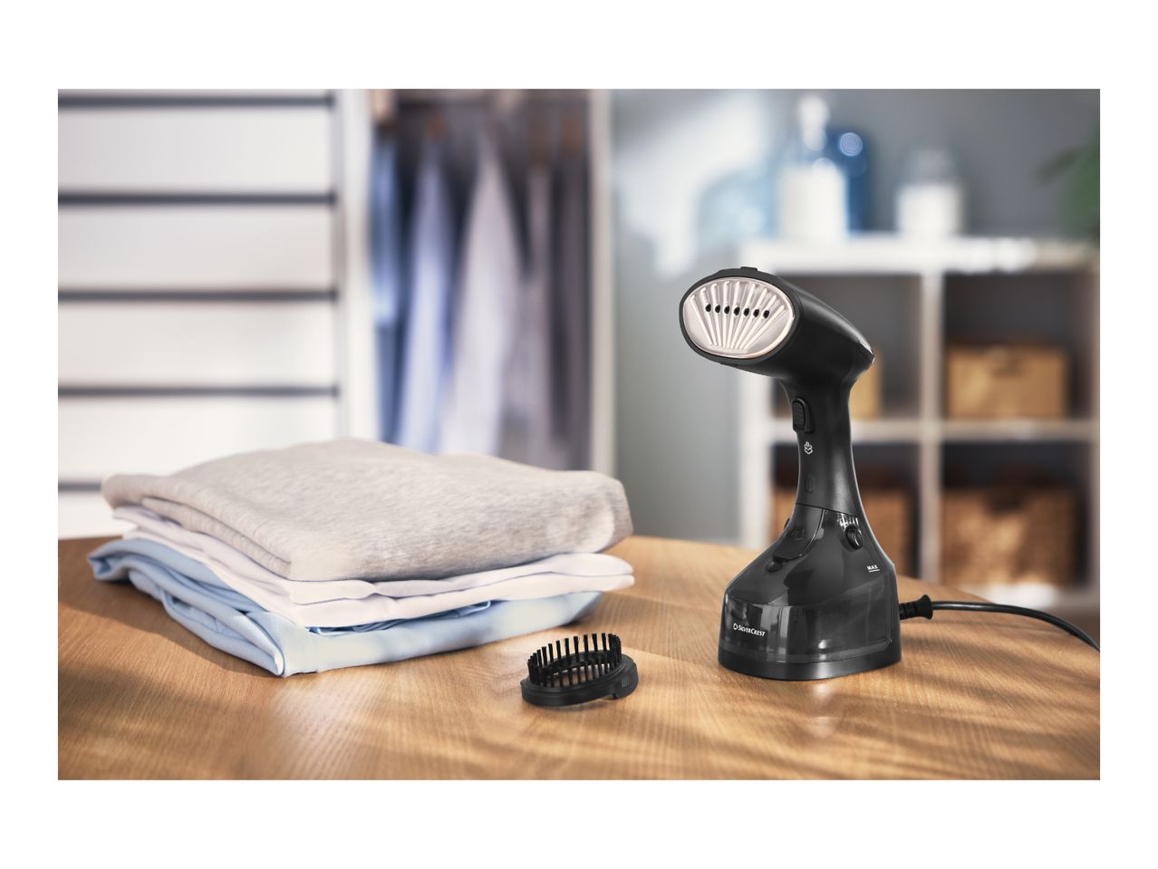 Handheld garment steamer with folded clothes on a wooden table.