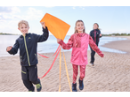 Twee kinderen in Lupilu softshell jassen rennen op het strand met een vlieger, een ander kind volgt.