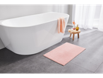 A pink LIVARNO home bath mat on a gray tiled floor next to a white bathtub.