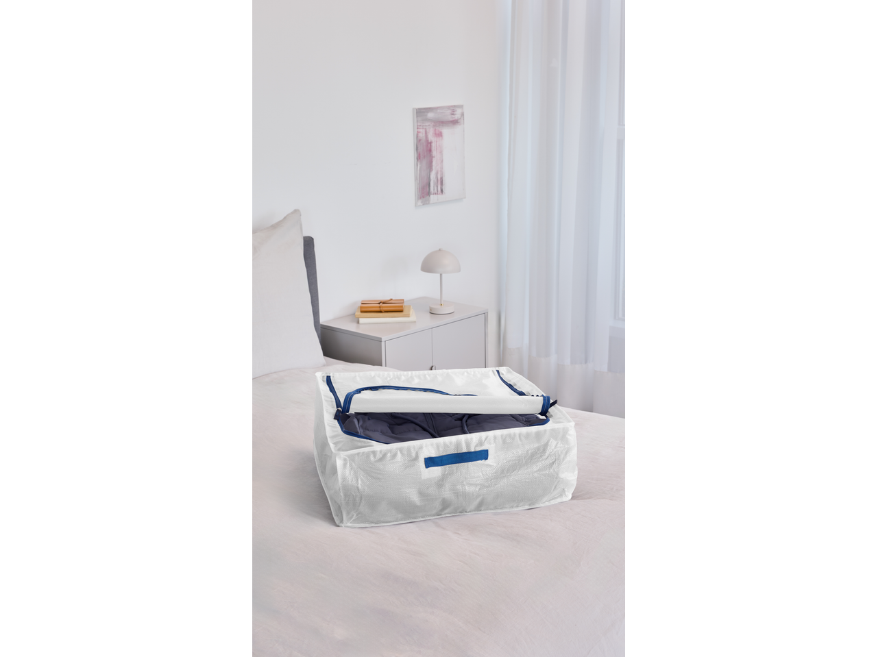 Saco de arrumação W5 branco com fecho azul, cheio de roupa, sobre uma cama.