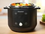 A black Breville pressure cooker sits on a kitchen counter with cooked vegetables inside.