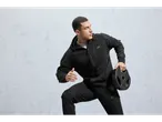 Uomo con felpa Crivit nera con cerniera e pantaloni della tuta che tiene un disco pesi.