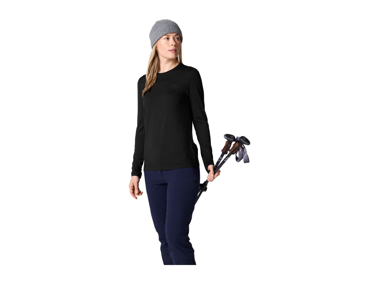 A woman in a black long-sleeved shirt, blue trousers, and a grey beanie holding trekking poles.